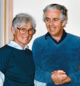 Man, with hands clasped, and woman standing against wall.